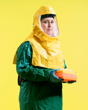 Researcher wearing a yellow and green hazmat suit, holding rectangular containers