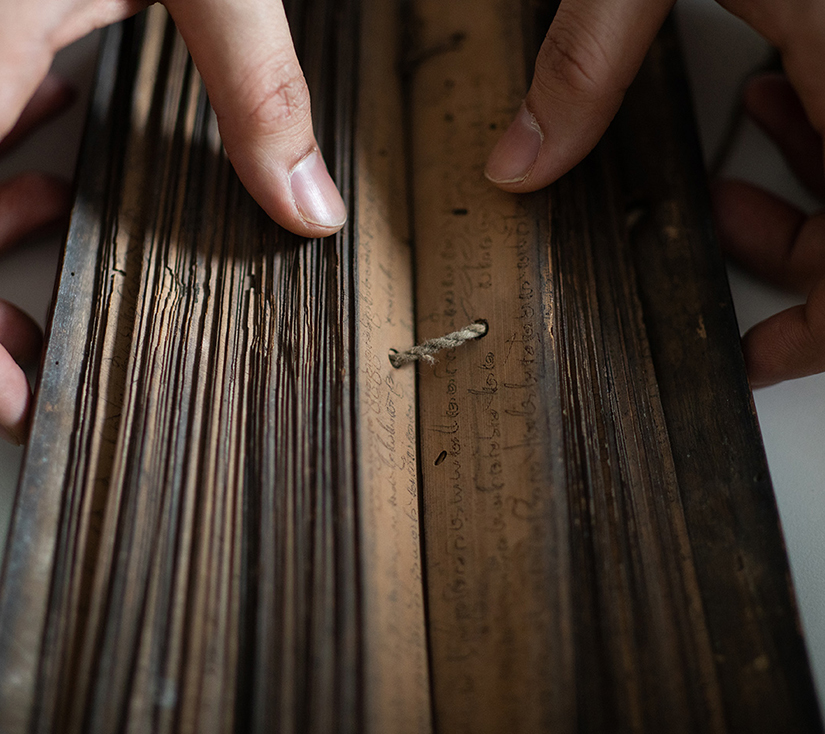 A pair of hands holding open two pages on the back of an ancient text, showing a string joining the pages