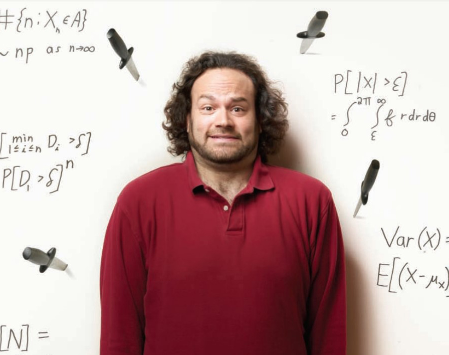 Jeffrey Rosenthal in a red long-sleeved shirt, smiling sheepishly at the camera, standing against a white wall peppered with mathematical formulae and surrounded by four knives stuck into the wall.