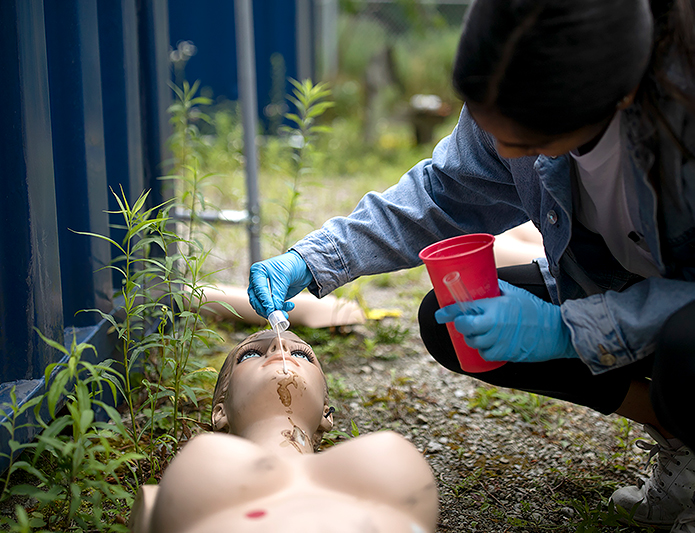 A student takes a swab of the brown stains on the chin of a bare, female-shaped dummy missing arms