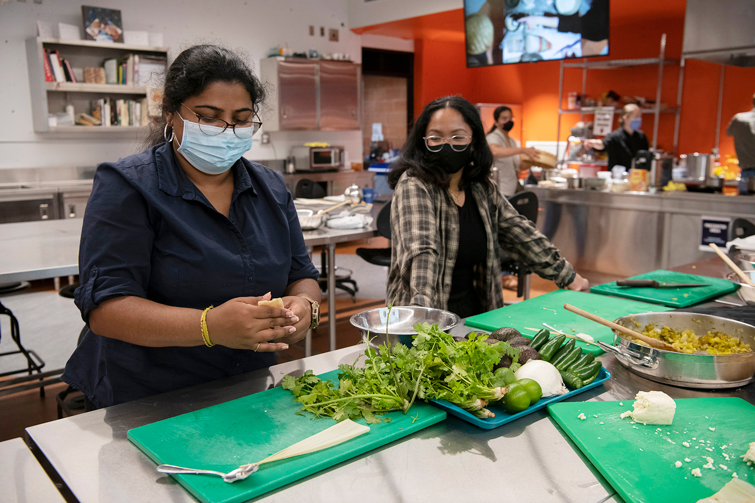 Two students, wearing face masks, prepare food in U of T Scarborough's kitchen lab, a tray of fresh cilantro, avocados, limes and other vegetables on the counter in front of them.