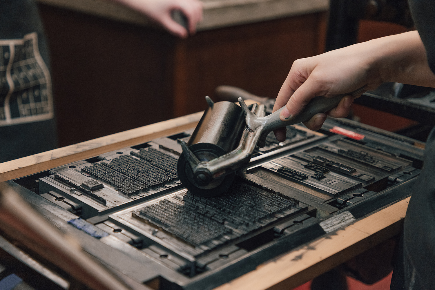 A small black ink roller moves over a tray of type, in preparation for printing.