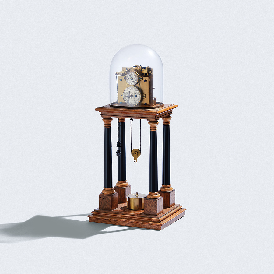 Hipp chronoscope with two dials inside a glass cover on top of a wooden platform above four columns and pulley with a hook hanging from the bottom. A weight rests on a second platform at the bottom.
