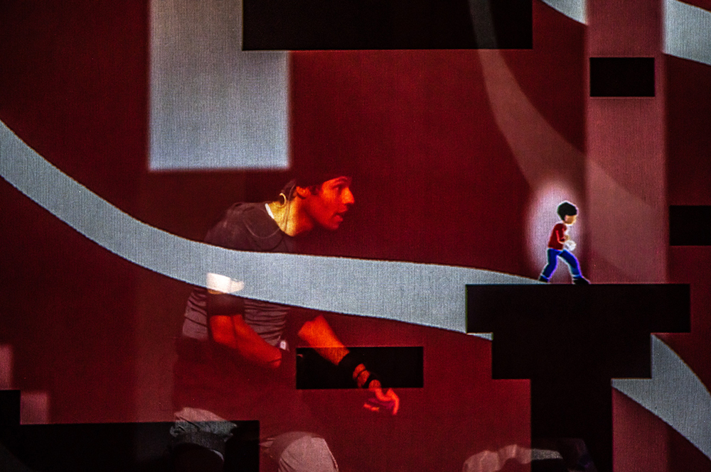 Side view of Sébastien Heins wearing motion capture equipment, with an animated 10-year-old version of himself depicted on a black platform in front of him.