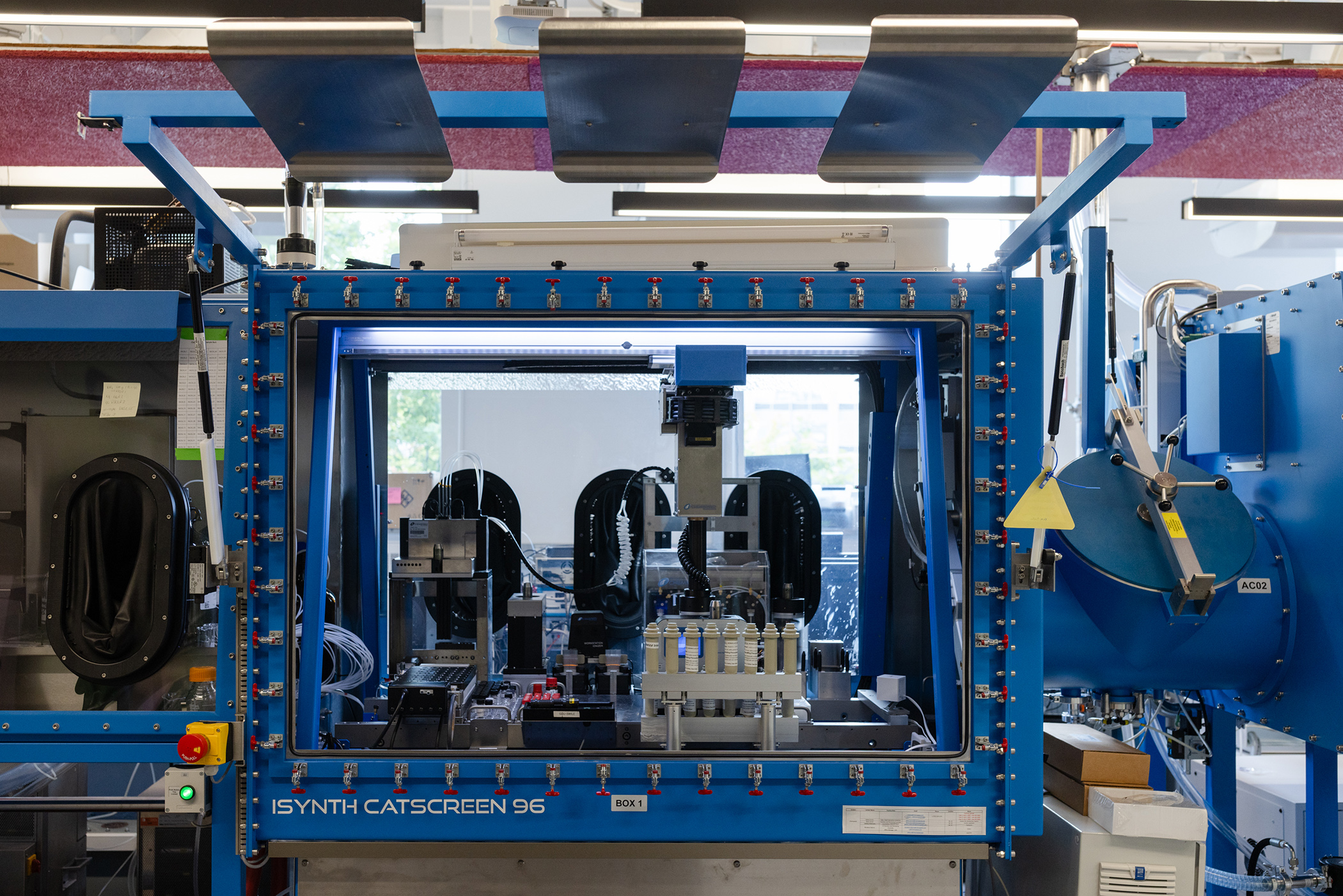An Isynth Catscreen 96, which is a piece of lab equipment that is robotic. It has a squarish blue metal frame and glass sides. Inside are tubes and a robotic arm