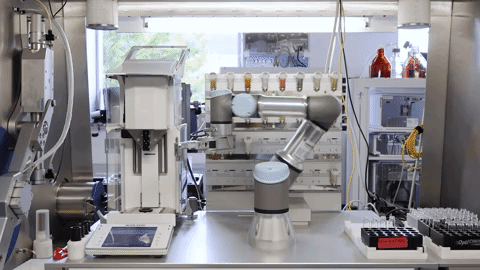 A robotic arm moves a vial from one part of a lab to another.