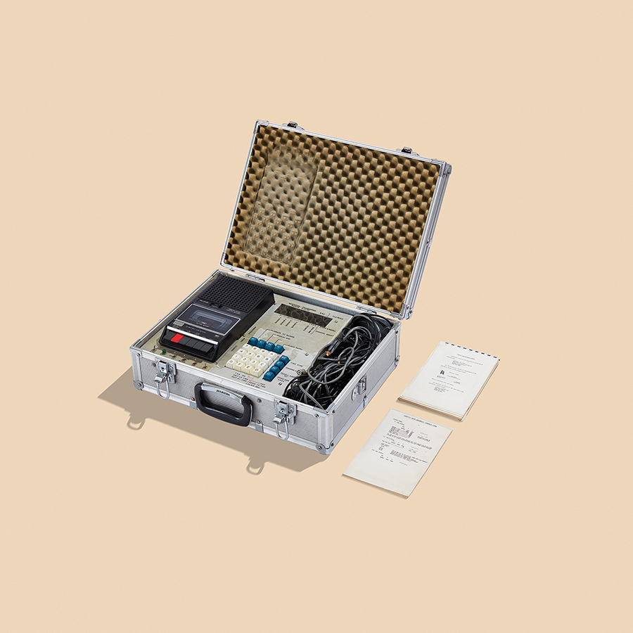 A steel suitcase box containing a tape recorder, a keypad on a console and a tangled pile of cables.