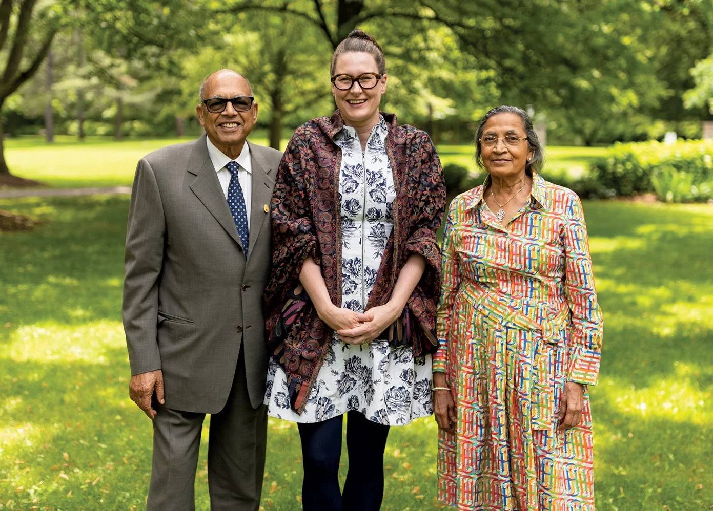 Outdoor photo of Gyan Jain on the left, Kanchan Jain on the right, and Alexandra Gillespie in the middle, standing in a grassy field surrounded by trees