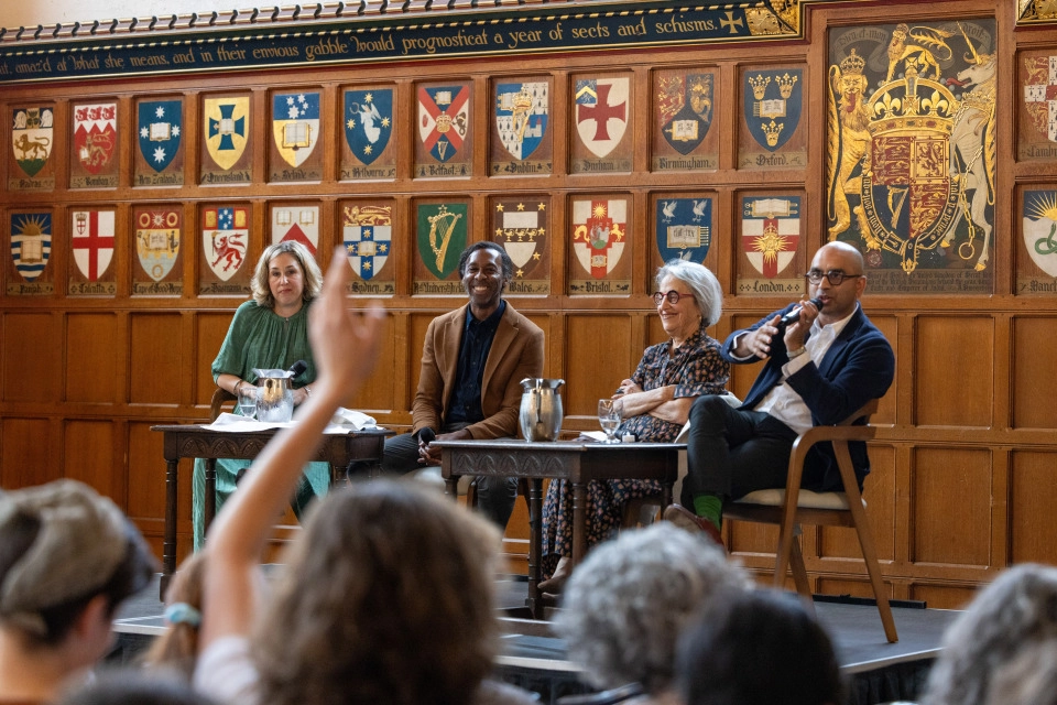 Four panellists are seated on a stage. Professor Randy Boyagoda is speaking into a microphone, responding to a question, and an audience member has one hand raised.