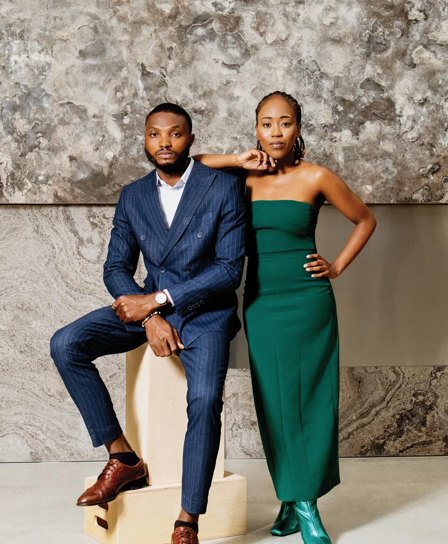 Mathew Okwoli in a blue, pin-striped suit, sitting on a wooden block on the left. Mahlodi Letsie in a green strapless gown standing on the right.