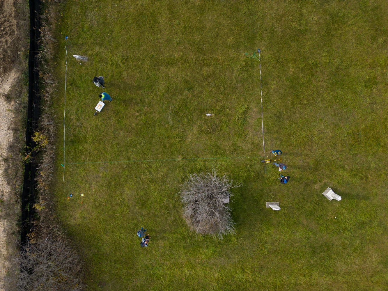 Bird's eye view of researchers surveying a grassy field with a square grid marked off