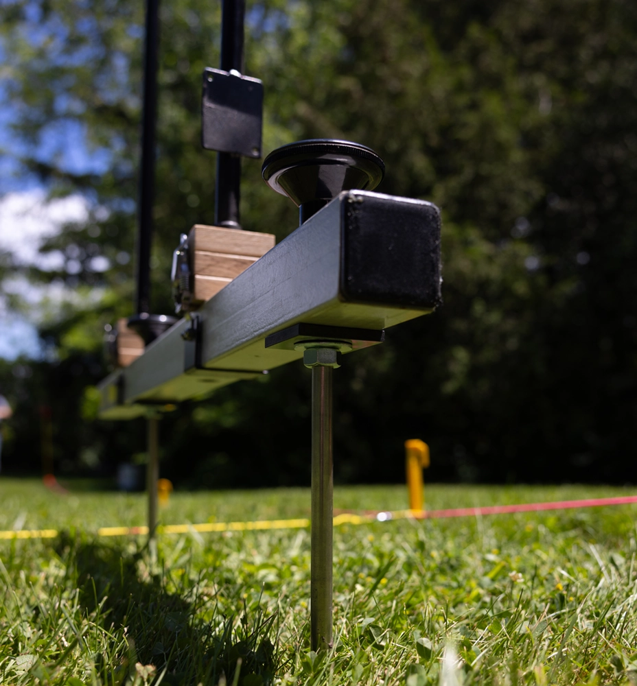 A measuring device consisting of a black bar attached to two rods inserted into a grassy field