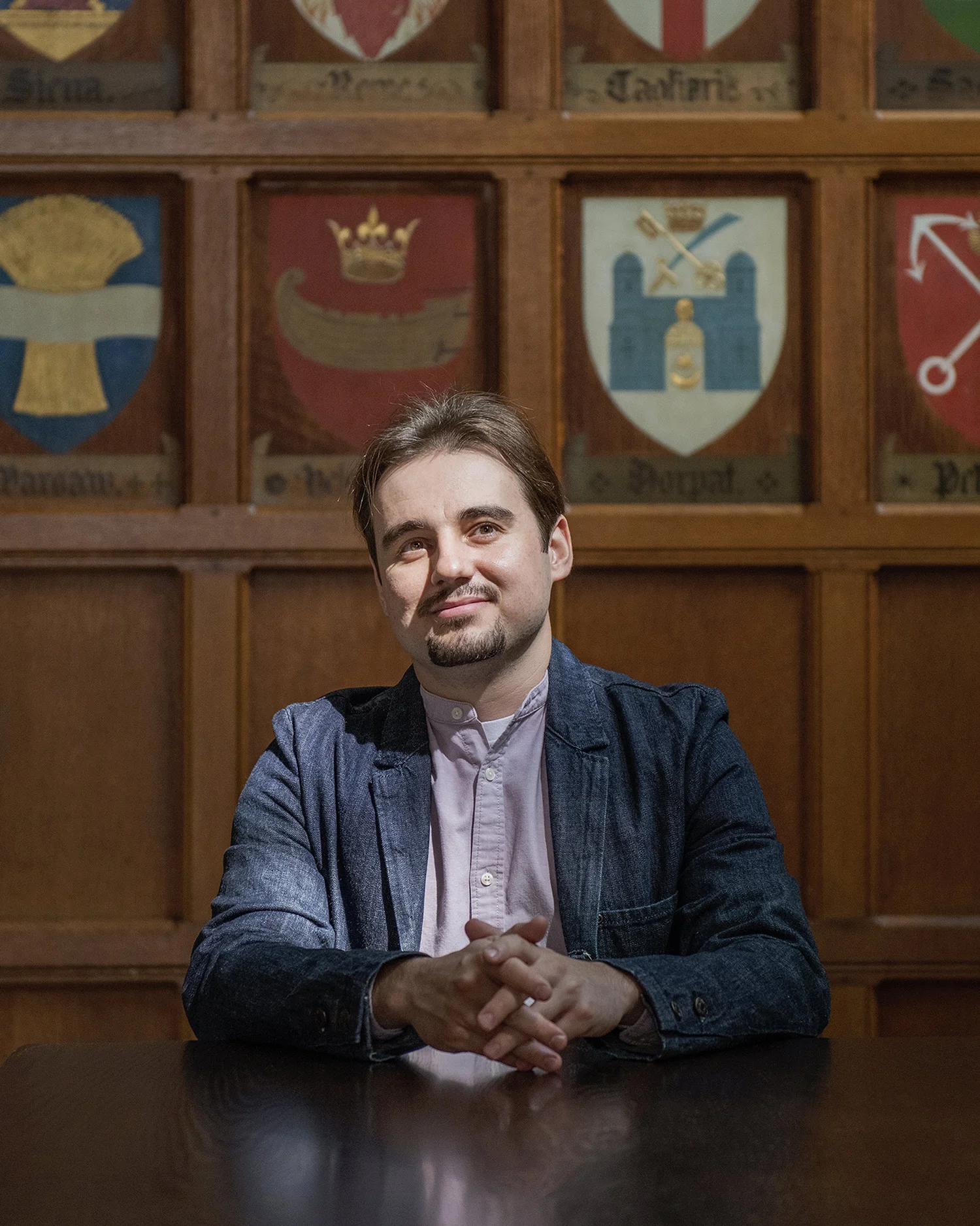 Vadym Lytvynov is seated behind a dark wooden table in front of a wood-panelled wall decorated with different coats of arms.