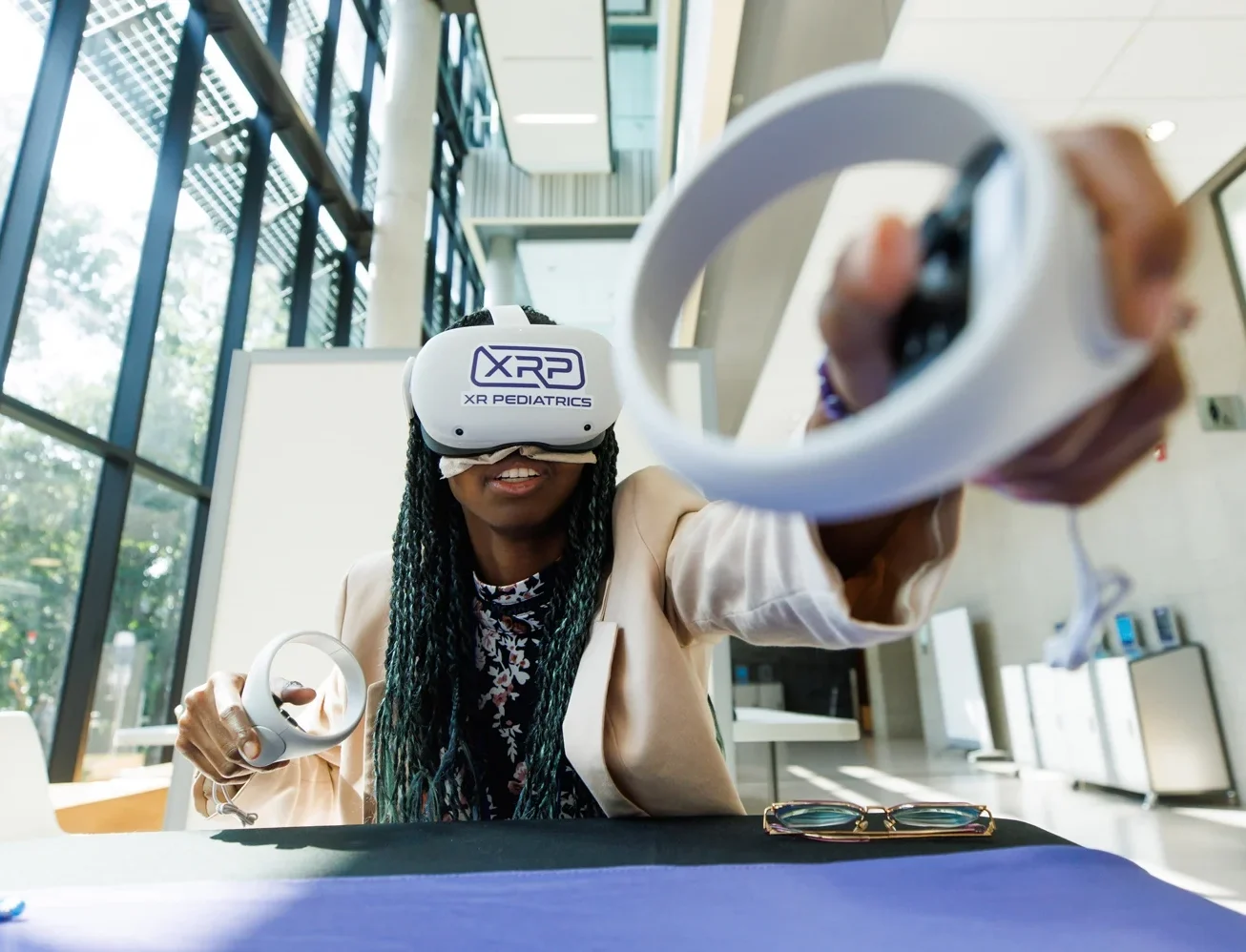 A woman has one arm stretched in front of her as she tries out an augmented reality simulation. She is wearing a headset and holding hand devices.