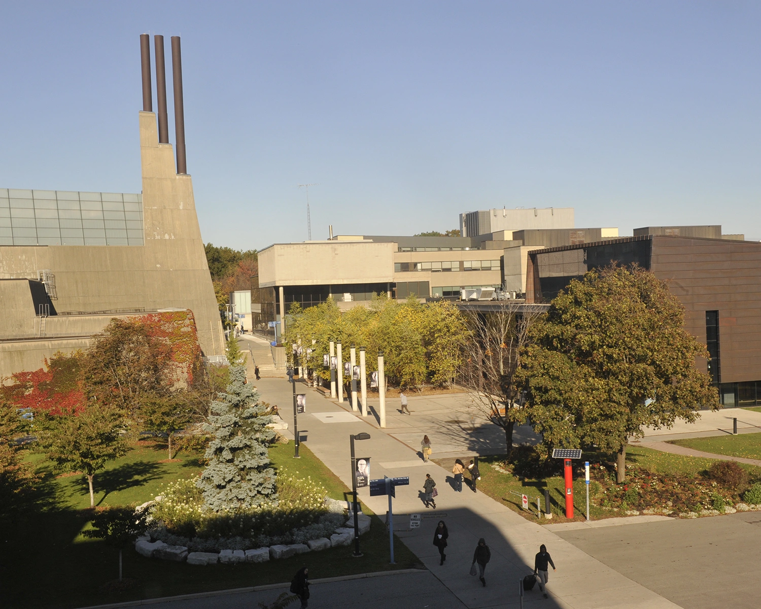 Bird's eye view of a walkway with a concrete, Brutalist-style building on the left and a copper-coloured building on the right