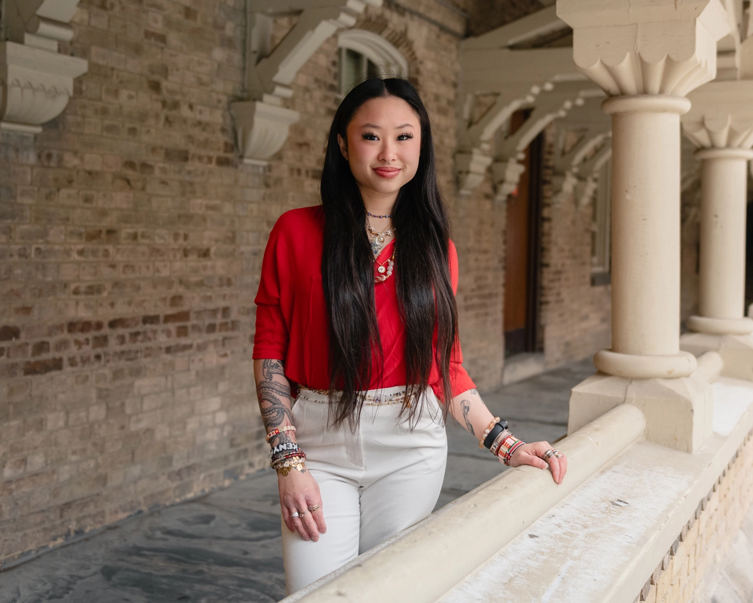 Xin Yi Lim, with bracelets, bangles and tattoos on her arms, is standing near an archway column at the University College Quad.