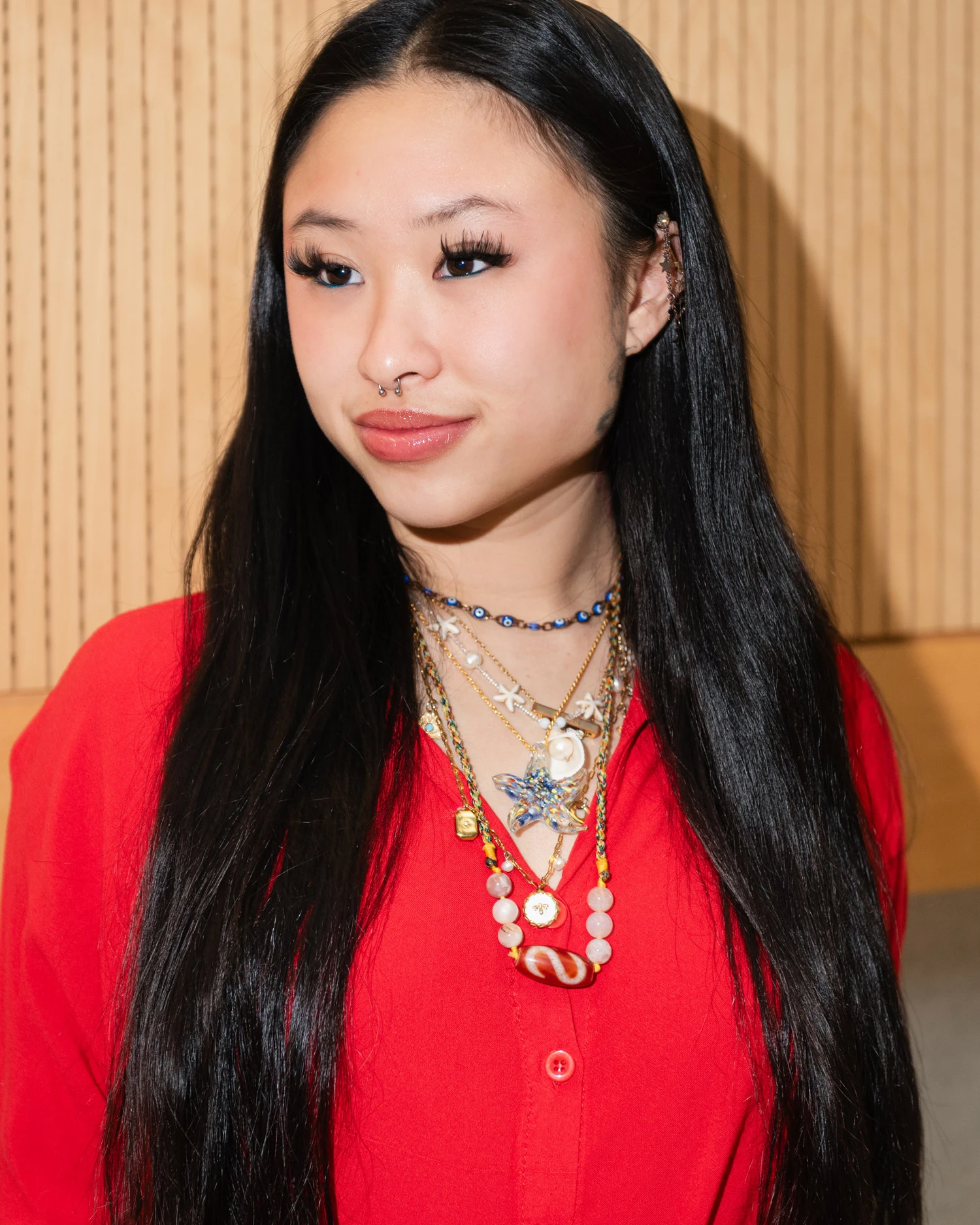 Close up of Xin Yi Lim, wearing a bold red shirt, a nose ring and multiple beaded necklaces