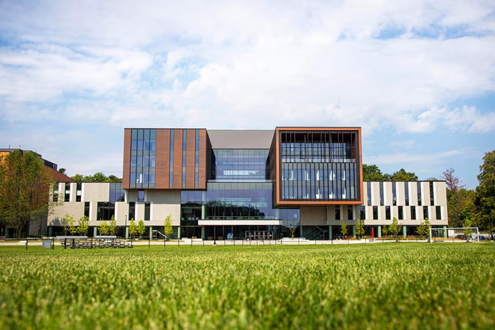 Exterior view of the Maanjiwe nendamowinan building at U of T Mississauga, with a grassy field in the foreground