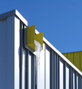 View from below of a wide, rectangular-shaped yellow gutter protruding slightly from the side of a building at the top