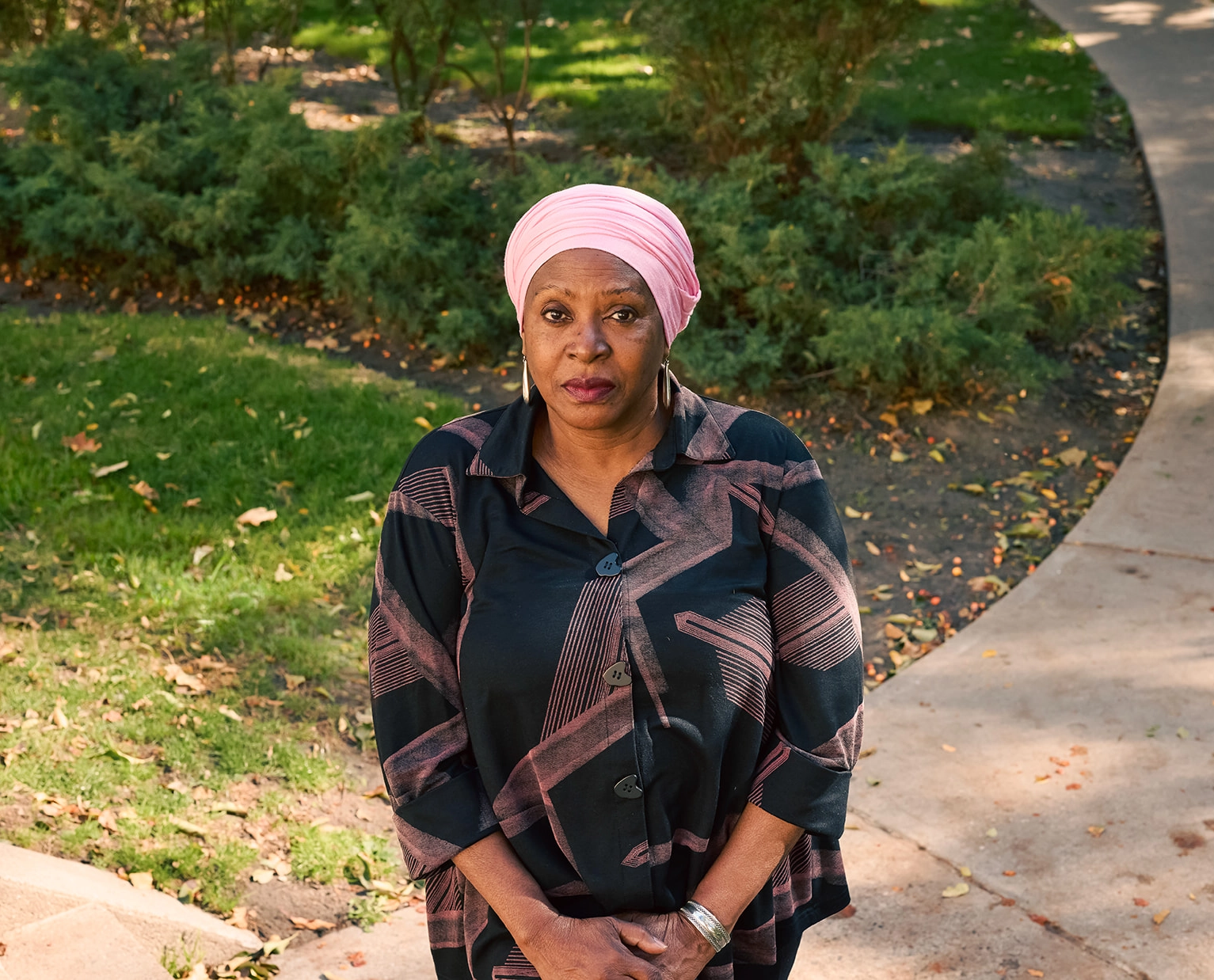 Prof. Afua Cooper, wearing a pink head wrap, standing on a winding concrete path in a park