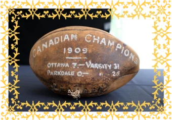 An old, faded football with the words Canadian Champions, 1909, Ottawa 7 -Varsity 31, Parkdale O - in white lettering on the ball