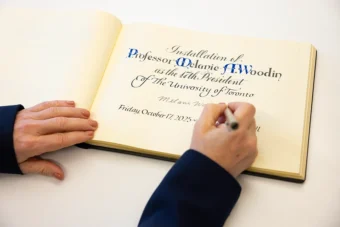 Close up of a hand signing a page of the president's installation book with the words: "Installation of Professor Melanie A. Woodin as the 17th President of The University of Toronto" and "Friday, October 17, 2025"