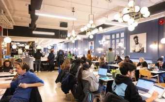 Students and a few staff are seated at every table in the Arbor Room. Some are working on their laptops, others are chatting or at the counter waiting for food.
