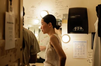 Side view of Judy Wang standing with other student actors in a theatre dressing room with the door open