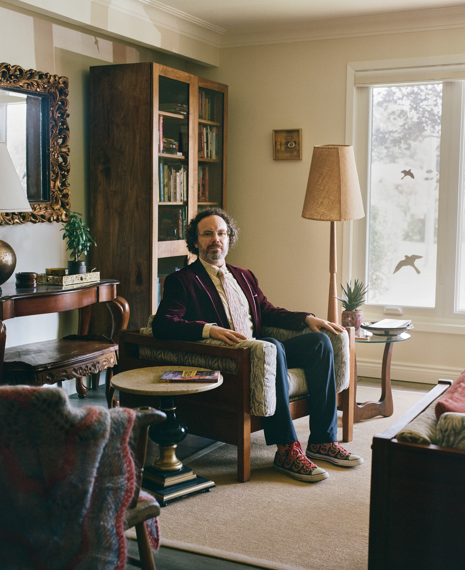 Photograph of Daniel Scott Tysdal seated in a room with bookshelves and a decorative mirror.